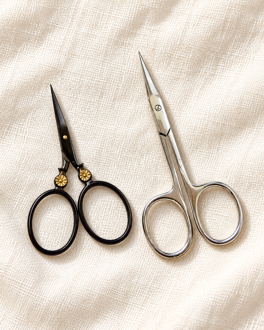 Moon Flower scissors with a black finish and gold floral rivets beside the silver Close Cut embroidery scissors on ivory linen.