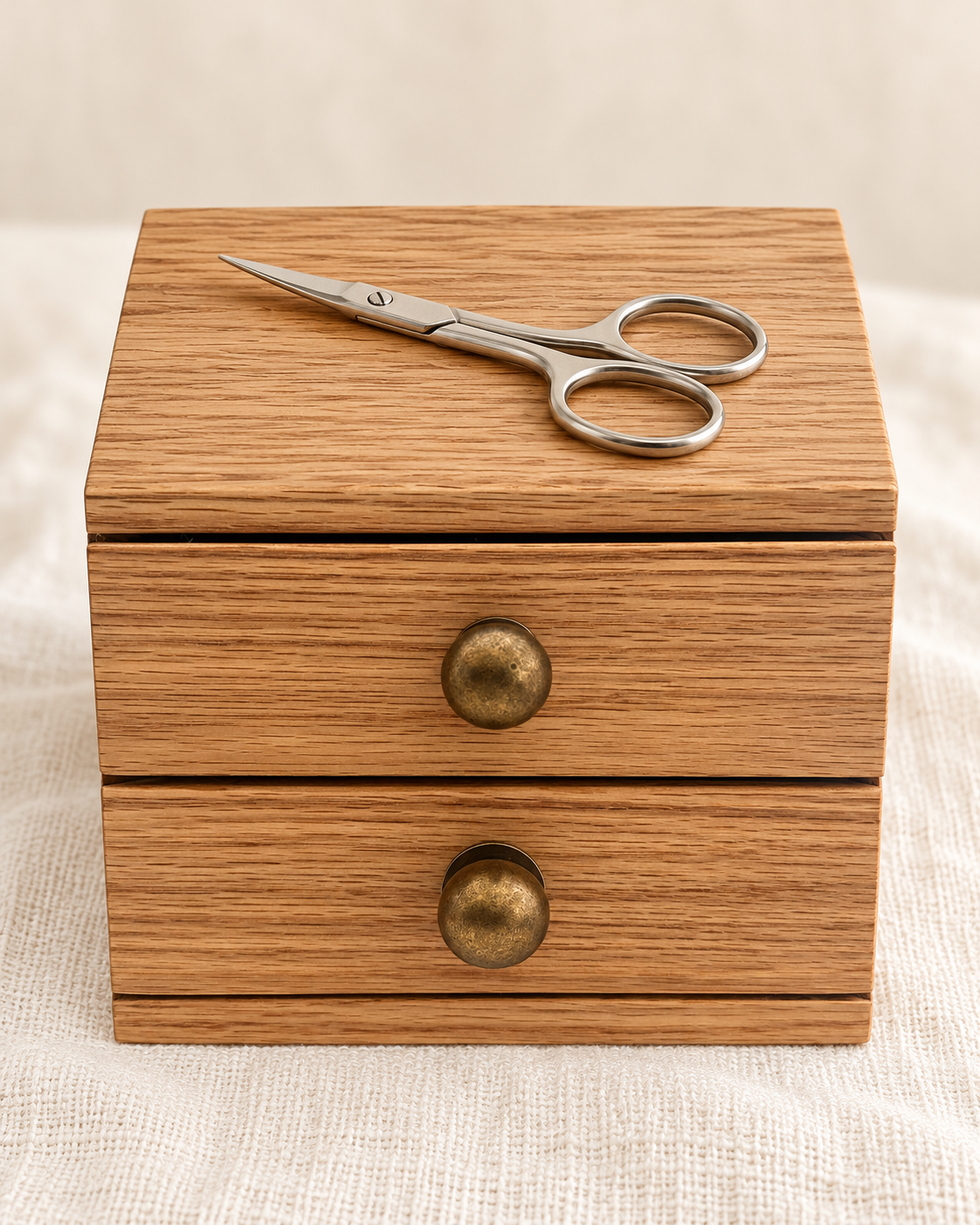 Wooden Two Drawer Chest with bronze knobs and the silver Close Cut embroidery scissors on its top, on ivory linen.
